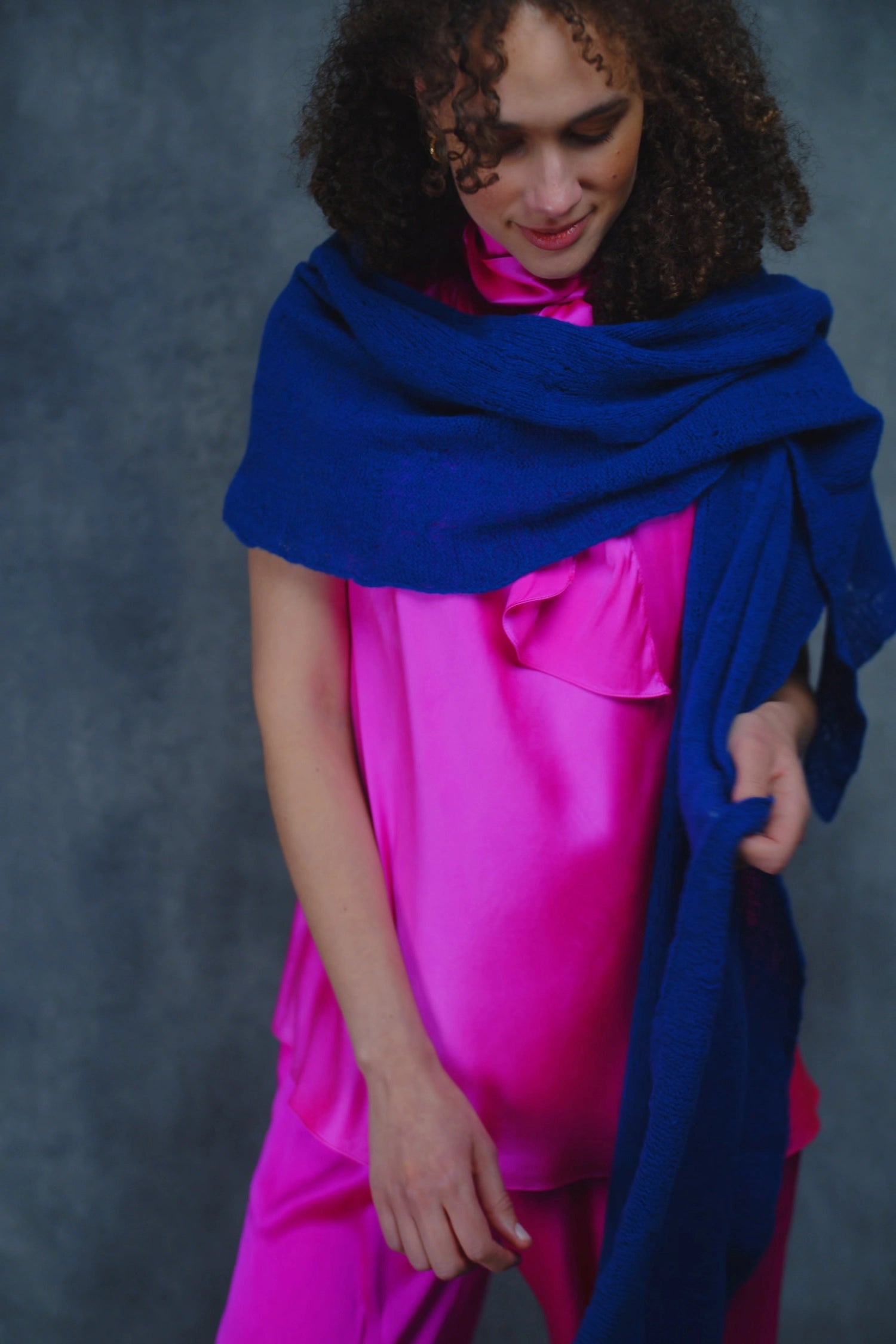 a woman wears a lace cashmere wrap shawl in indigo blue over her bright pink silk clothing
